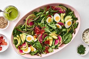 cobb salad with hard boiled egg, pancetta, veggies, avocado, goat cheese & sunflower seeds next to a jar of herb vinaigrette