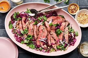 steak salad with thai dressing on a serving platter made with red cabbage, mint, cilantro, shallots and roasted peanuts