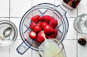 lime juice being poured in a blender with simple syrup, strawberries, tequila, and orange liquor