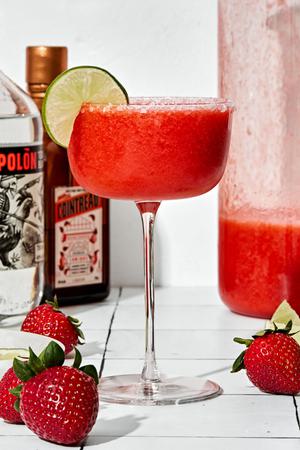 a blended strawberry margarita in a salt rimmed glass garnished with a lime slice