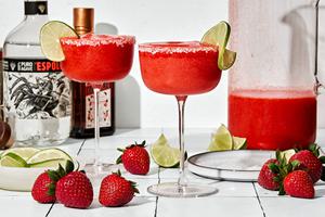 2 blended strawberry margaritas in a salt rimmed glasses garnished with a lime slice