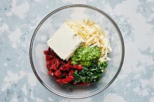cooked spinach, garlic, cream cheese, mozzarella, sun-dried tomatoes, and pesto in a mixing bowl