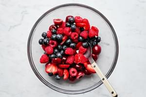 fresh strawberries, blueberries, raspberries and chopped cherries being stirred together in a bowl