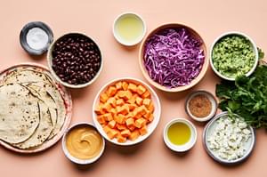 sweet potatoes, black beans, corn tortillas, quick slaw, vegan queso, vegan crumbles, guacamole and cilantro in prep bowls