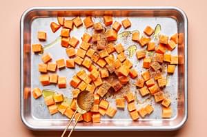 cubed sweet potatoes being tossed with olive oil and taco seasoning on a baking shet