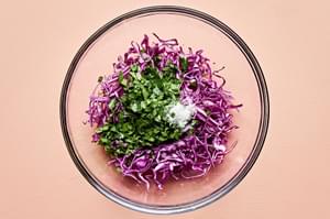 finely shredded cabbage, cilantro, lime juice and salt being tossed in a bowl to make quick slaw