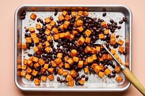 roasted sweet potatoes seasoned with taco seasoning being tossed with black beans on a baking sheet