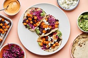 sweet potato tacos topped with cabbage slaw, vegan goat cheese, guacamole and a drizzle of vegan queso