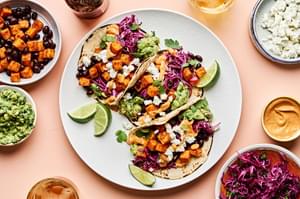 sweet potato tacos topped with cabbage slaw, vegan goat cheese, guacamole and a drizzle of vegan queso