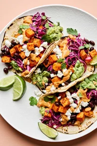 sweet potato tacos topped with cabbage slaw, vegan goat cheese, guacamole and a drizzle of vegan queso