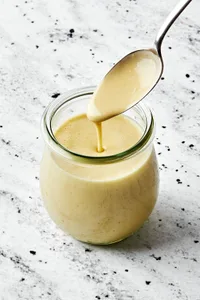 homemade tahini dressing in a jar with a spoon made with  tahini, olive oil, apple cider vinegar,, sesame oil, honey & spices