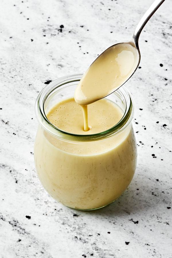 homemade tahini dressing in a jar with a spoon made with tahini, olive oil, apple cider vinegar,, sesame oil, honey & spices