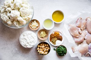 cauliflower in a bowl next to chicken thighs, garlic, yogurt, olive oil and chickpeas