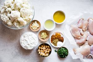 cauliflower in a bowl next to chicken thighs, garlic, yogurt, olive oil and chickpeas
