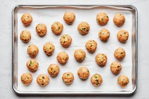 raw meatballs made with ground chicken, eggs, panko, spices, green onions, and sesame oil on a parchment lined baking sheet