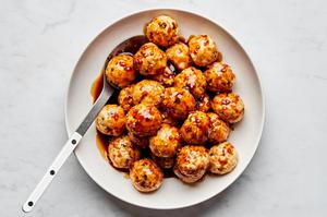 a large serving bowl full of homemade teriyaki meatballs with a serving spoon