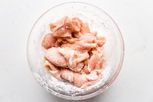 thinly sliced chicken in a bowl coated with corn starch