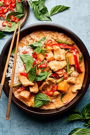 A bowl of chicken Thai red curry served over fluffy jasmine rice, featuring a rich, creamy sauce with vibrant vegetables