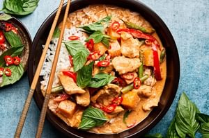 A bowl of chicken Thai red curry served over fluffy jasmine rice, featuring a rich, creamy sauce with vibrant vegetables