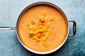 cubed pumpkin simmering in a pan of cream thai red curry sauce