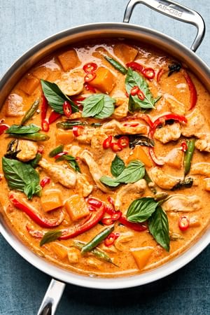 a pan of creamy thai red curry with chicken and vegetables topped with fresh thai basil