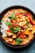 A bowl of Thai red curry with chicken and vegetables served over fluffy jasmine rice, topped with fresh thai basil