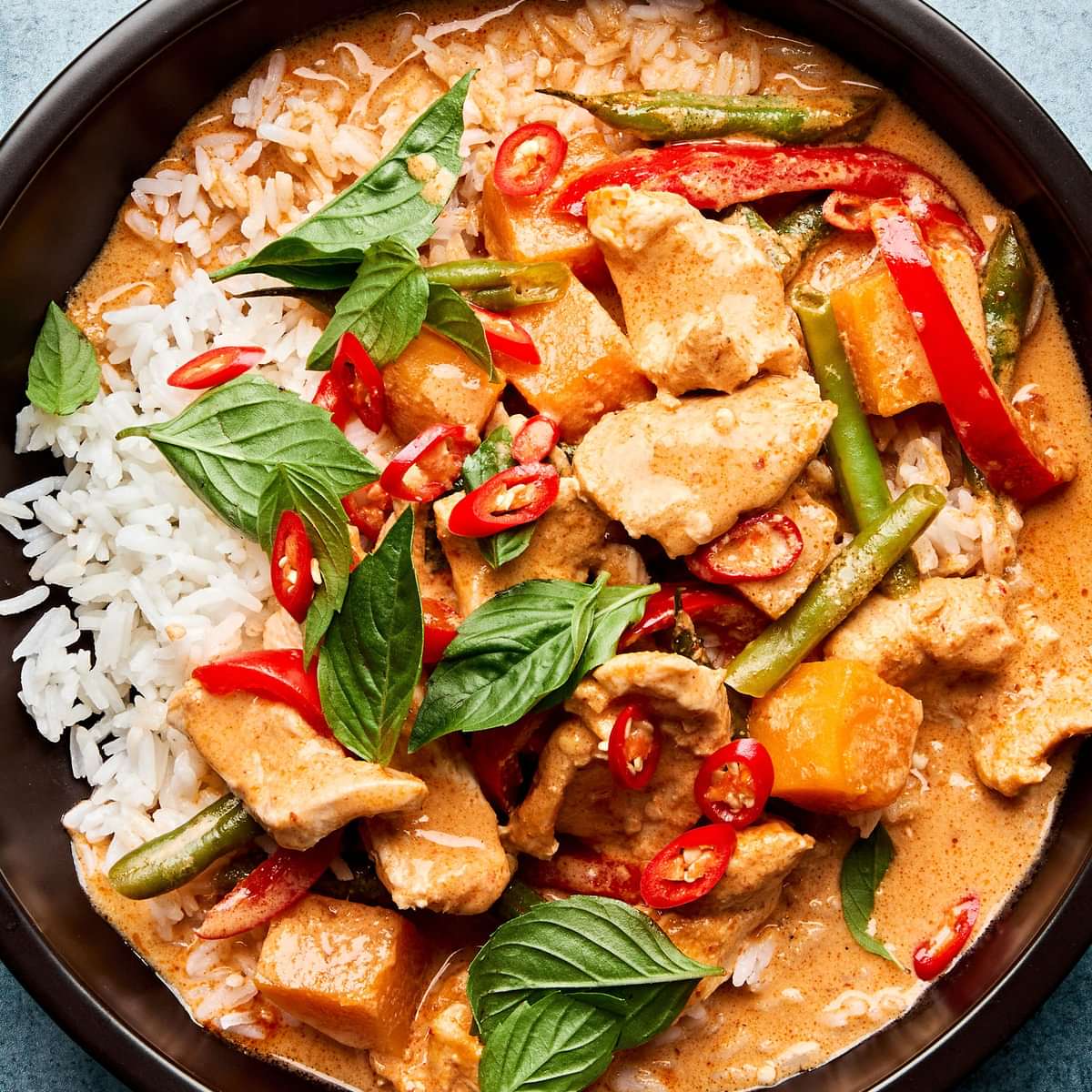 A bowl of Thai red curry with chicken and vegetables served over fluffy jasmine rice, topped with fresh thai basil