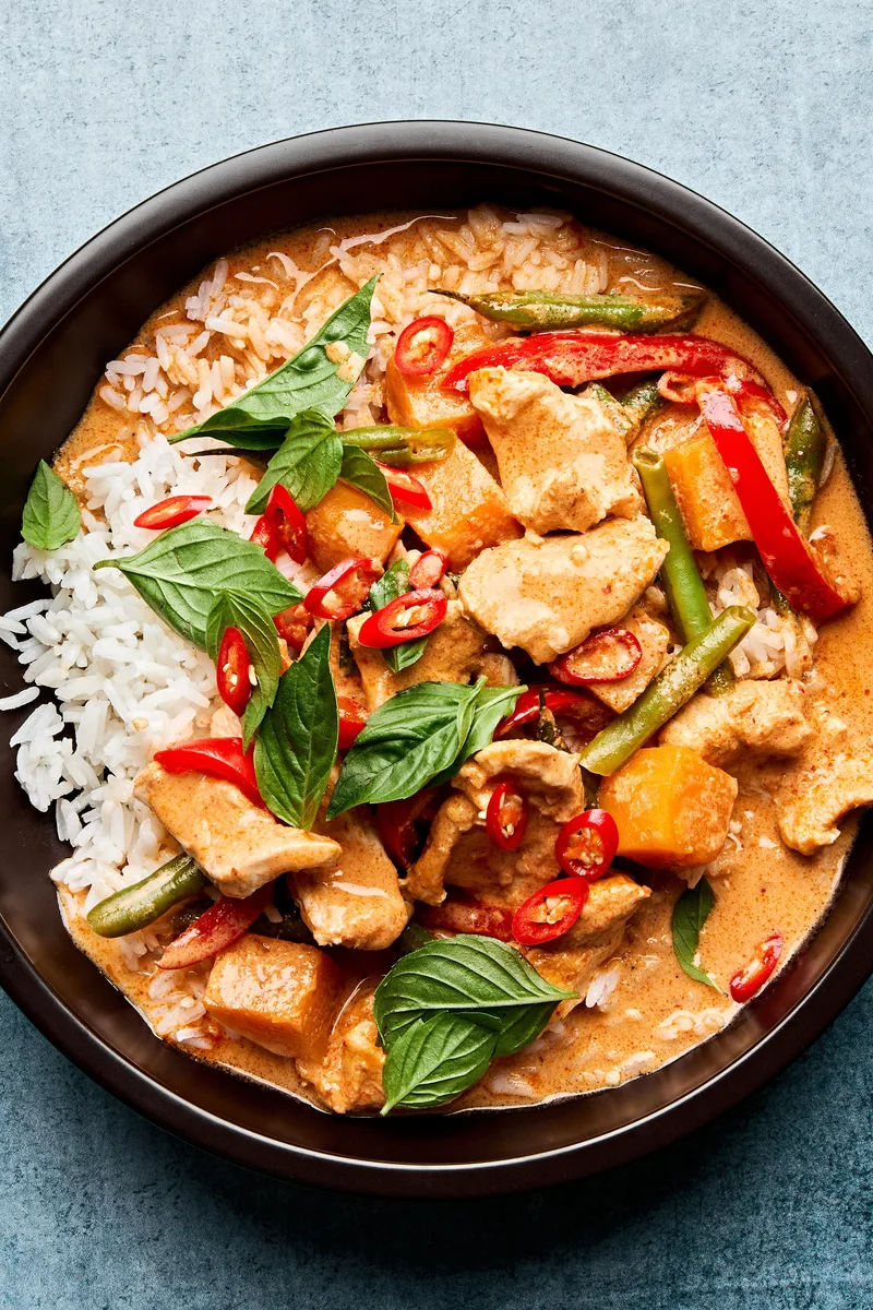 A bowl of Thai red curry with chicken and vegetables served over fluffy jasmine rice, topped with fresh thai basil