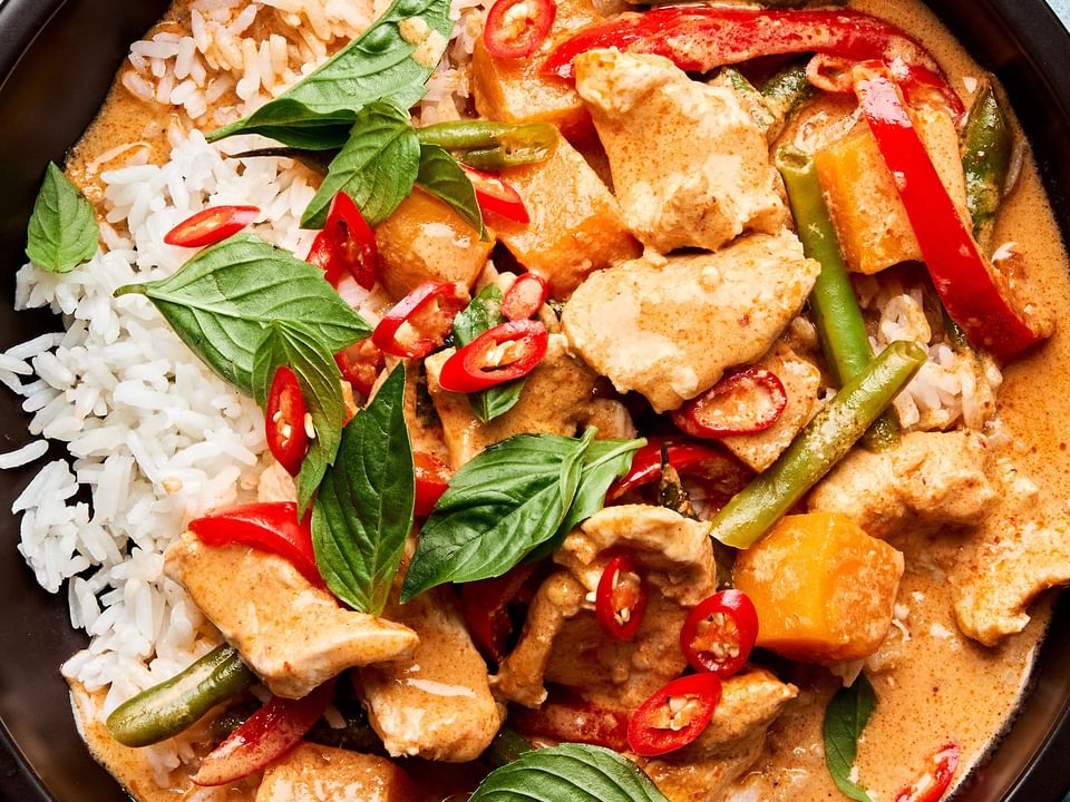 A bowl of Thai red curry with chicken and vegetables served over fluffy jasmine rice, topped with fresh thai basil