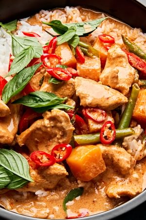 A bowl of Thai red curry with chicken and vegetables served over fluffy jasmine rice, topped with fresh thai basil