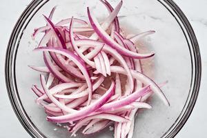 thinly sliced red onion being tossed with vinegar and garlic