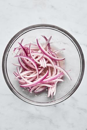 thinly sliced red onion being tossed with vinegar and garlic