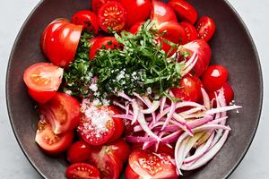 marinated red onion, tomatoes, olive oil, salt, parsley, basil, garlic, onion and vinegar being tossed in a bowl