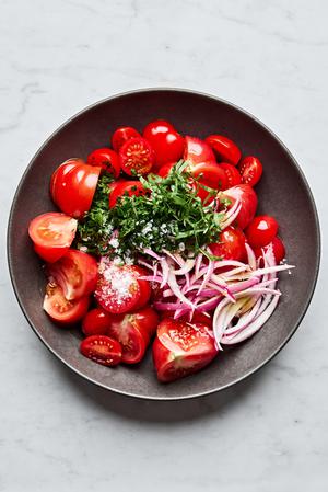 marinated red onion, tomatoes, olive oil, salt, parsley, basil, garlic, onion and vinegar being tossed in a bowl