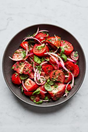 tomato salad made with marinated onions, tomatoes, olive oil, salt, parsley, basil, garlic, onion and vinegar.