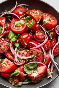 tomato salad made with marinated onions, tomatoes, olive oil, salt, parsley, basil, garlic, onion and vinegar.