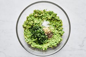 avocado mashed in a bowl with lemon juice, garlic, basil, salt, and pepper.
