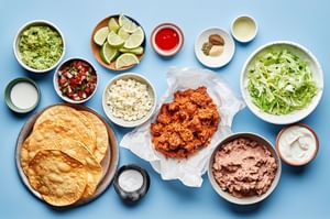 ingredients laid out for easy tostadas: tostada shells, chorizo, beans, guacamole, pico de gallo, sour cream and spices