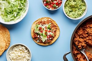 toppings being piled on a crispy corn tortilla to make easy tostadas with chorizo, beans, lettuce, pico and lime crema