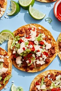 Easy tostadas with chorizo, refried beans, lettuce, cotija, pico de gallo, guac, and lime crema on crispy shells