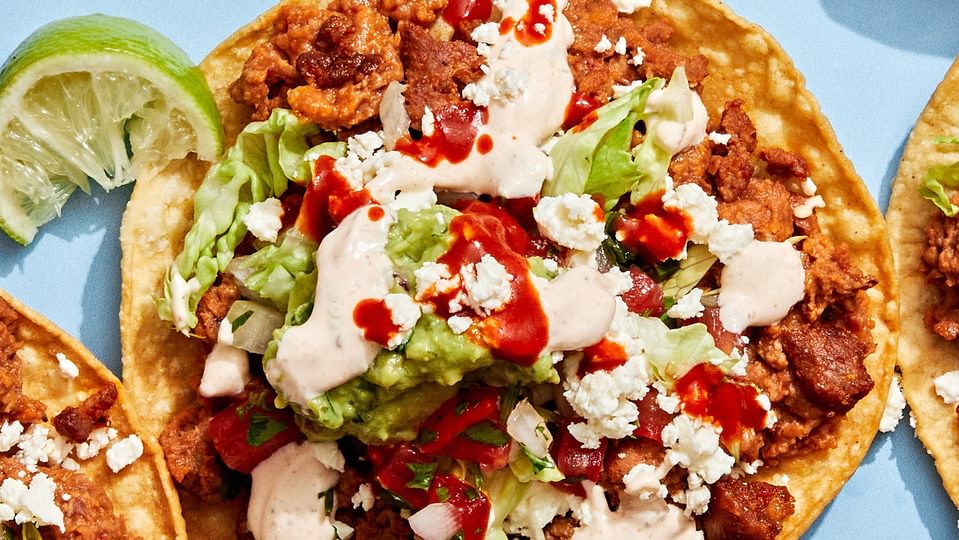 Easy tostadas with chorizo, refried beans, lettuce, cotija, pico de gallo, guac, and lime crema on crispy shells