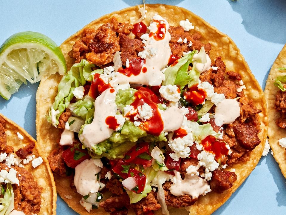 Easy tostadas with chorizo, refried beans, lettuce, cotija, pico de gallo, guac, and lime crema on crispy shells