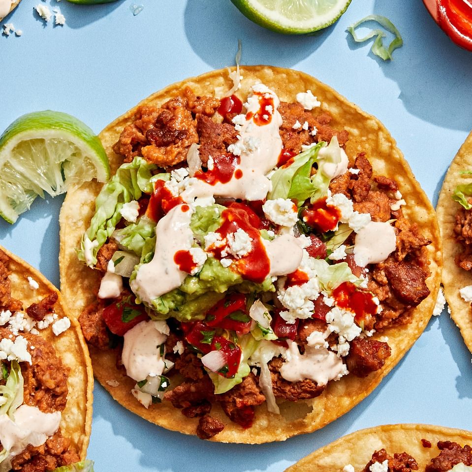 Easy tostadas with chorizo, refried beans, lettuce, cotija, pico de gallo, guac, and lime crema on crispy shells