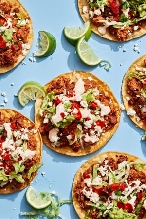 Easy tostadas with chorizo, refried beans, lettuce, cotija, pico de gallo, guac, and lime crema on crispy shells