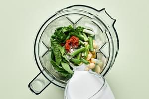coconut milk, curry paste, cilantro, mint, salt, macadamia nuts, lime juice, and green onions being added to a blender