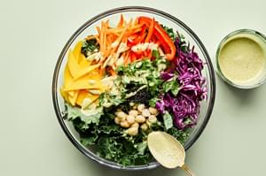 kale, mango, red cabbage, mint, cilantro, bell pepper, carrots, macadamia nuts being drizzled with creamy dressing