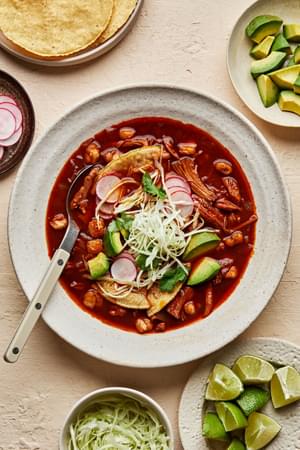 a bowl of homemade turkey pozole rojo topped with seasoned cabbage, avocado, cilantro, radishes, and lime juice.