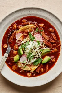 a bowl of homemade turkey pozole rojo topped with seasoned cabbage, avocado, cilantro, radishes, and lime juice.