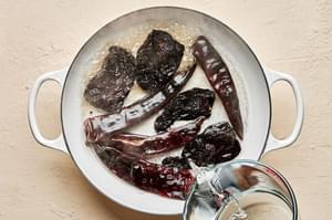 hot water being poured over dried chilis in a skillet