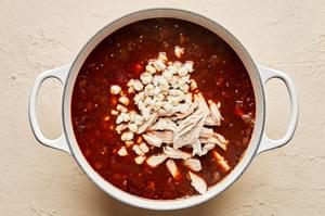 turkey added to a soup pot with onions, blended chiles, stock, cumin, oregano, bay leaves and salt